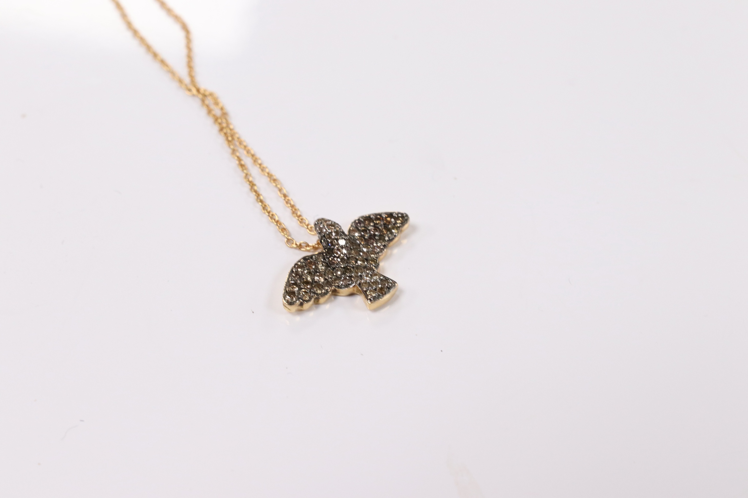 A modern 18k and pave set two colour diamond chip bird pendant, wing span 19mm, on an Italian 18k fine link chain, 36cm, gross weight 4.4 grams. Condition - fair to good